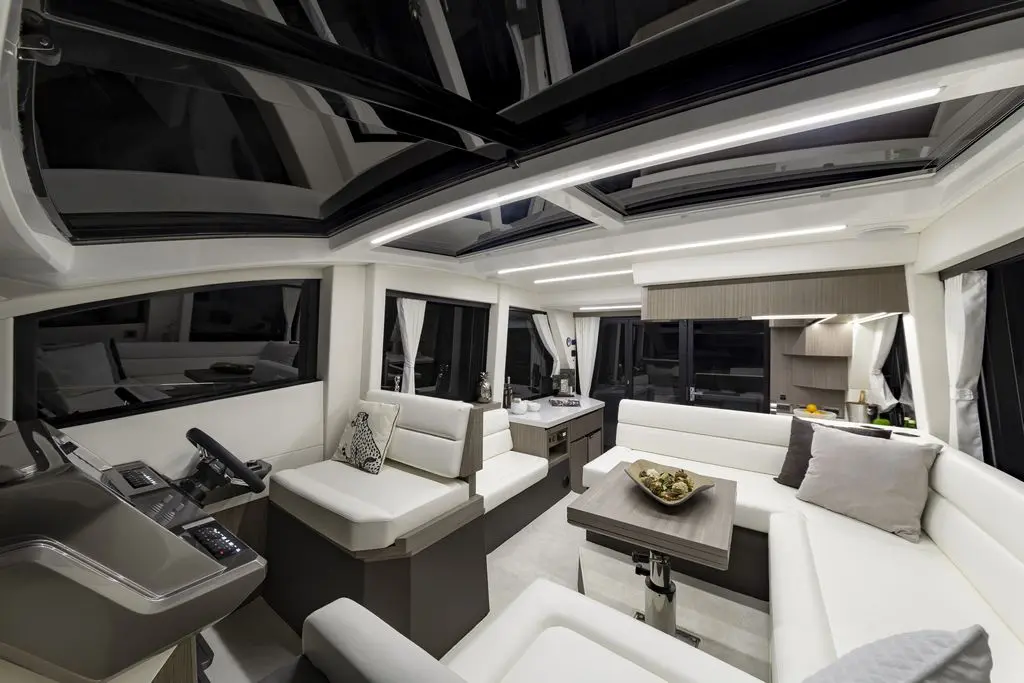 Stylish yacht interior with white seating, modern helm, and large windows; features a sleek table and elegant decor.