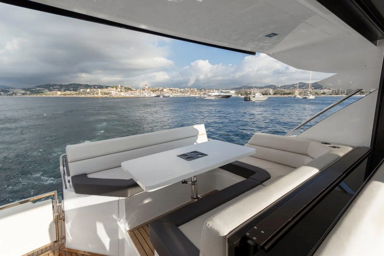 Luxurious yacht seating area with a white table, overlooking a coastal town and calm waters under a partly cloudy sky.