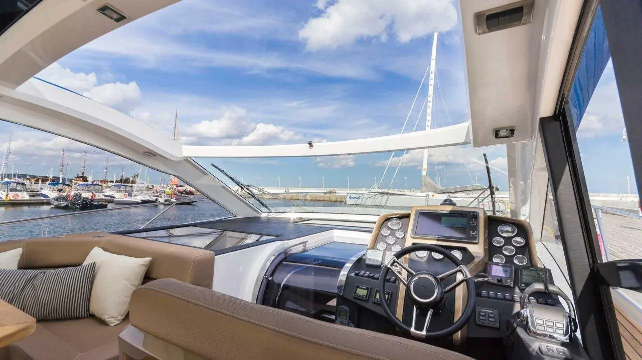 Luxury yacht interior featuring steering wheel, control panel, and marina view under a blue sky with scattered clouds.