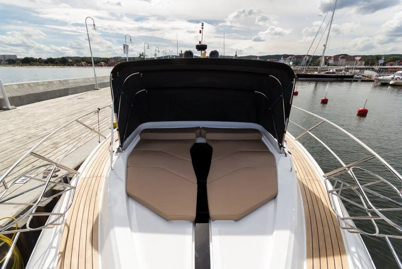 A luxury boat's deck featuring plush tan cushions, with a marina and cloudy sky visible in the background.