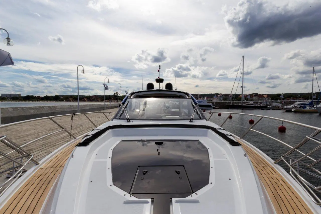 View from the bow of a luxury yacht, showcasing a wooden deck, marina, boats docked, and a cloudy sky.