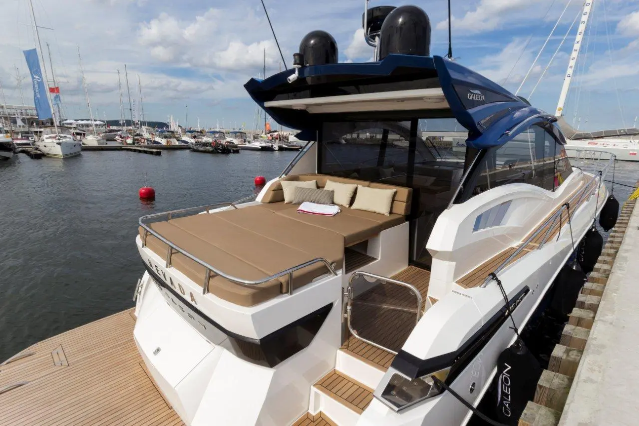 Luxury motor yacht with a spacious sunbathing area, plush cushions, and views of a bustling marina in the background.