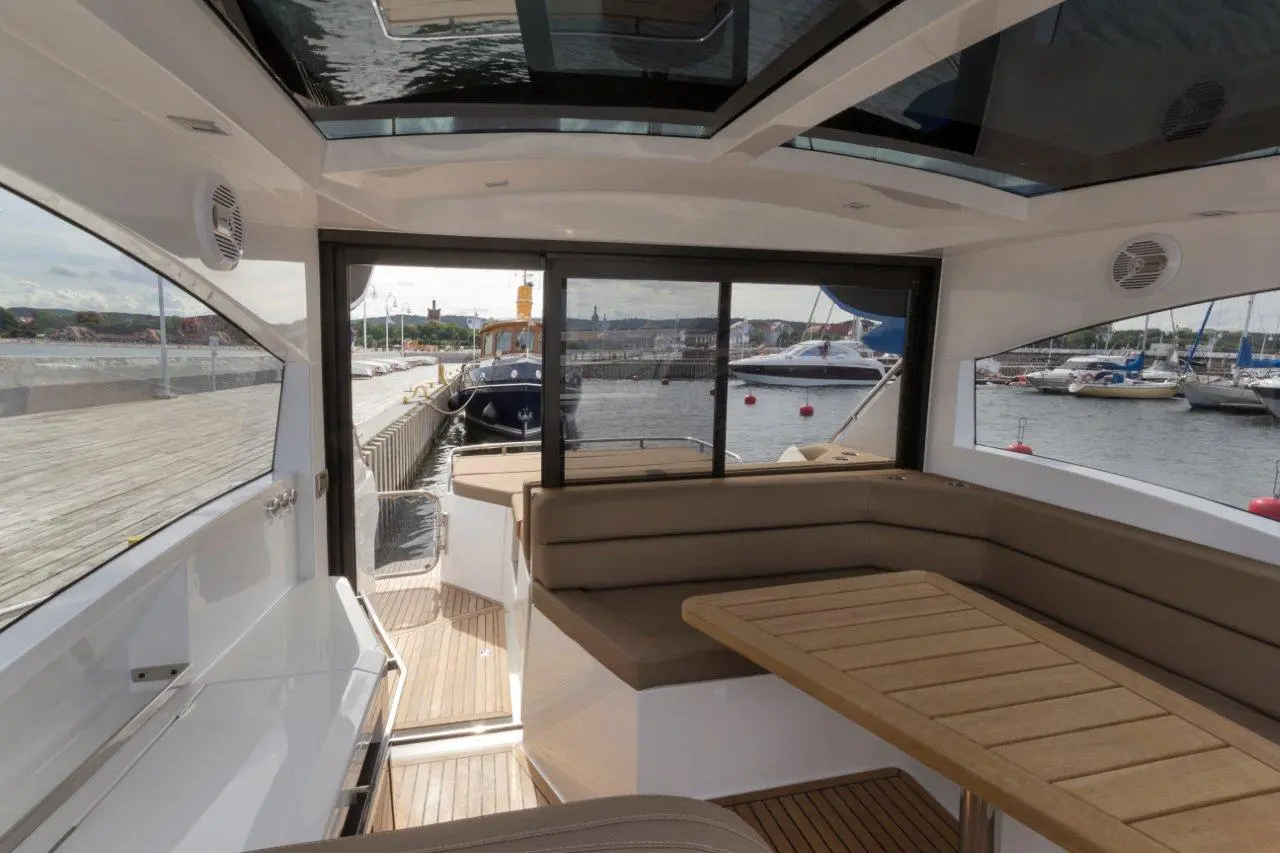 Interior view of a modern boat with a wooden table, leather seating, and panoramic windows overlooking a marina.