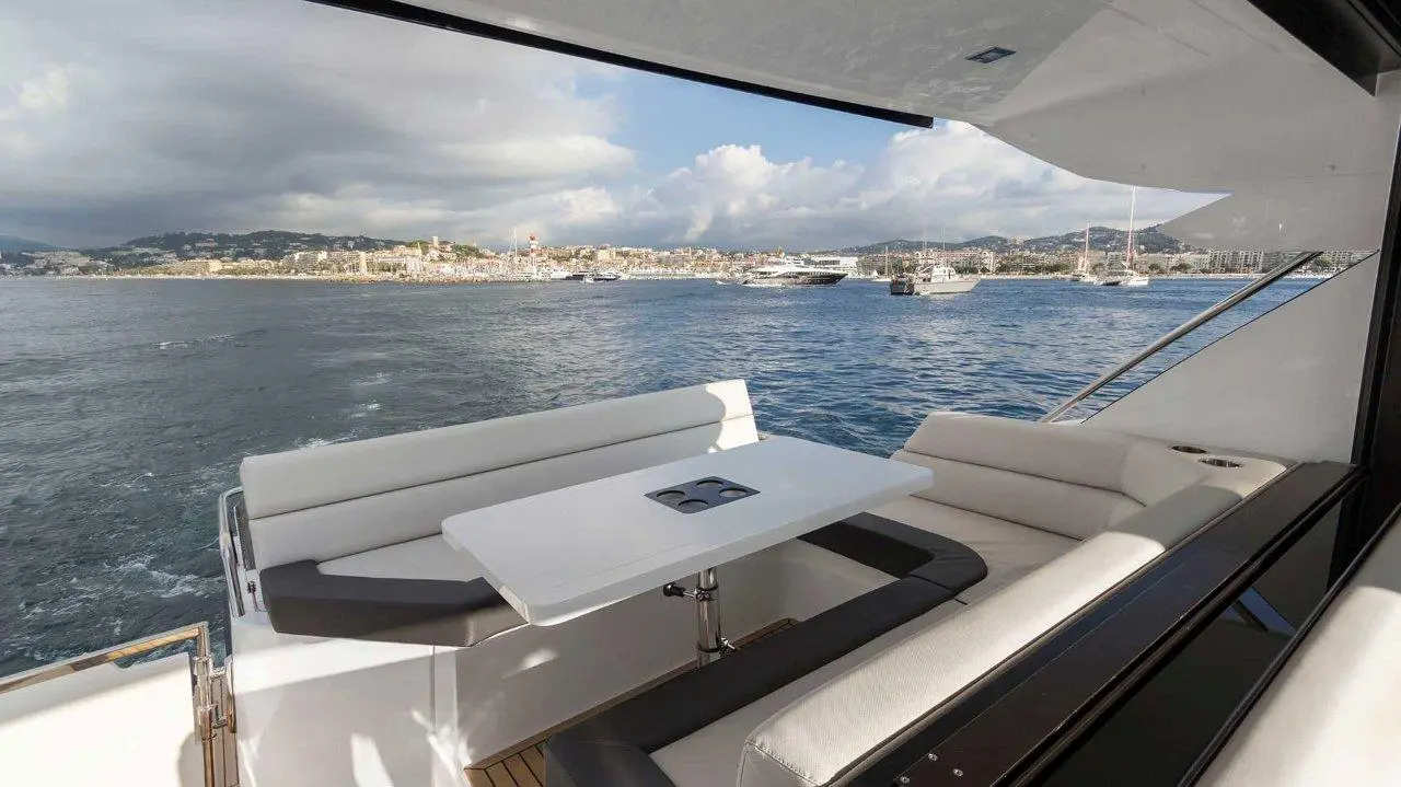 Luxury yacht deck with a white table and seating, overlooking boats in the harbor and a cloudy sky in the background.