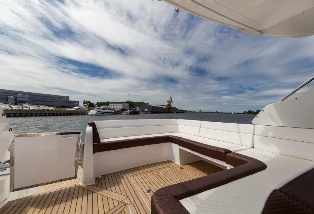 Luxury yacht deck with comfortable seating overlooking the water, blue sky with clouds, and marina in the background.