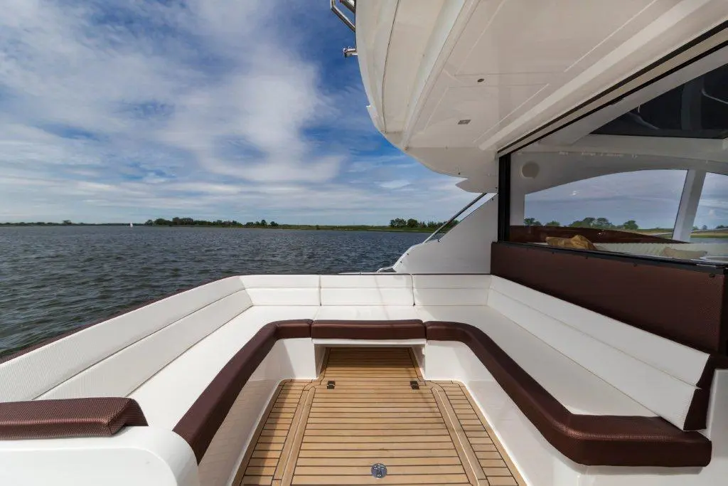Luxurious boat deck with white seating, wooden floor, and scenic water view under a blue sky with clouds.
