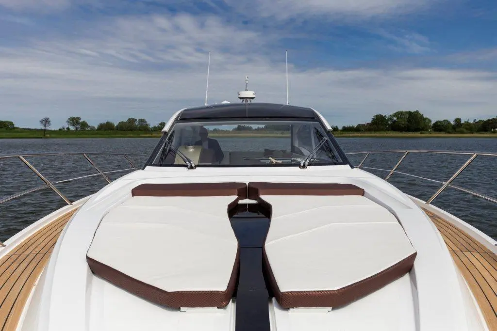 Luxury yacht bow with cushioned seating, overlooking calm water and greenery under a partly cloudy sky.