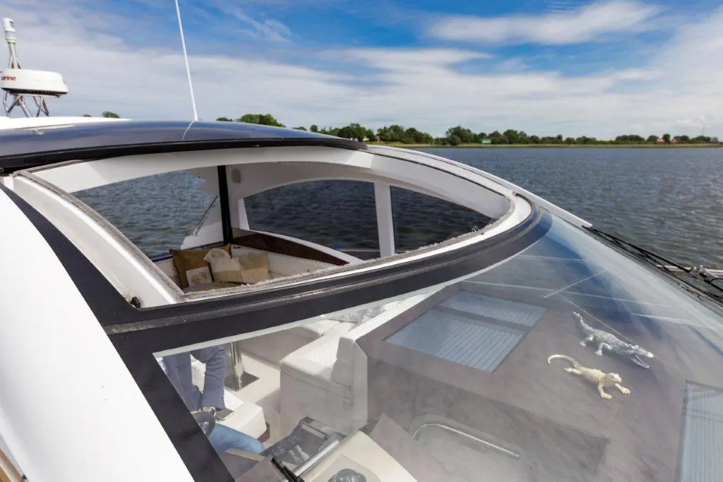 Interior view of a luxury boat's helm with a river background, featuring plush seating and toy alligators on the dashboard.
