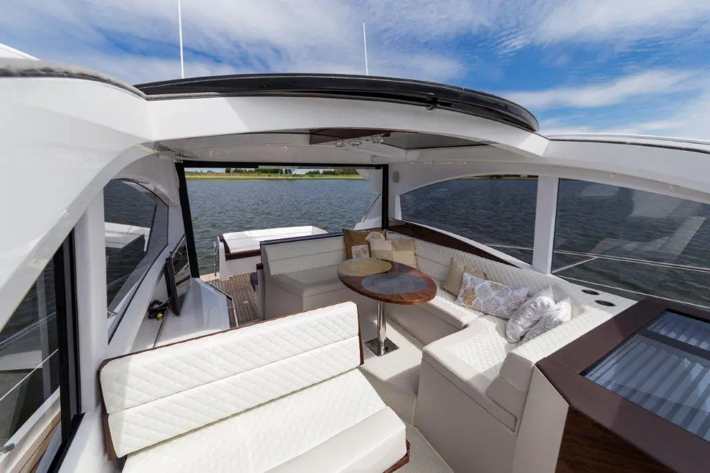 Luxury boat interior featuring a white seating area and a round table by the water, with blue sky above.