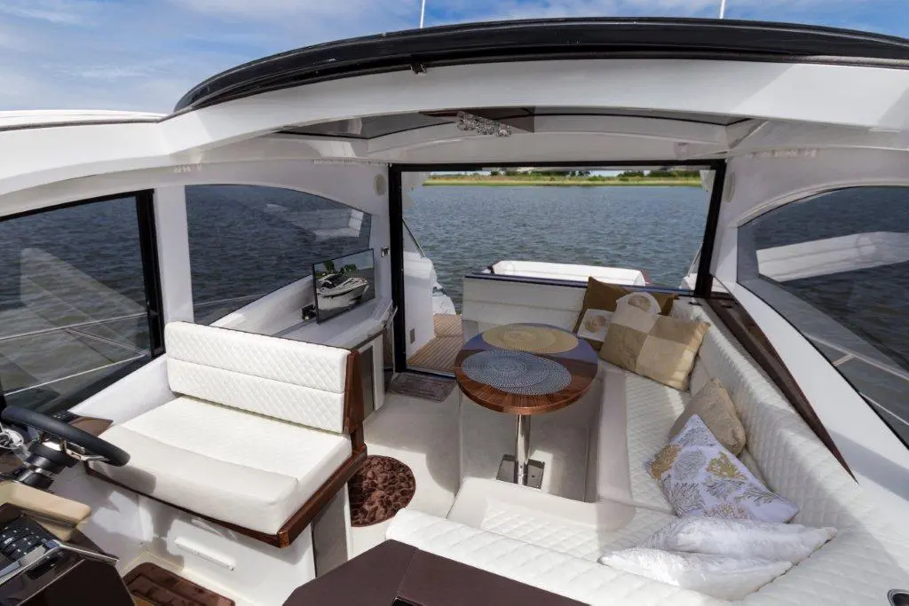 Modern boat interior featuring a plush seating area, a round wooden table, and scenic water views through large windows.