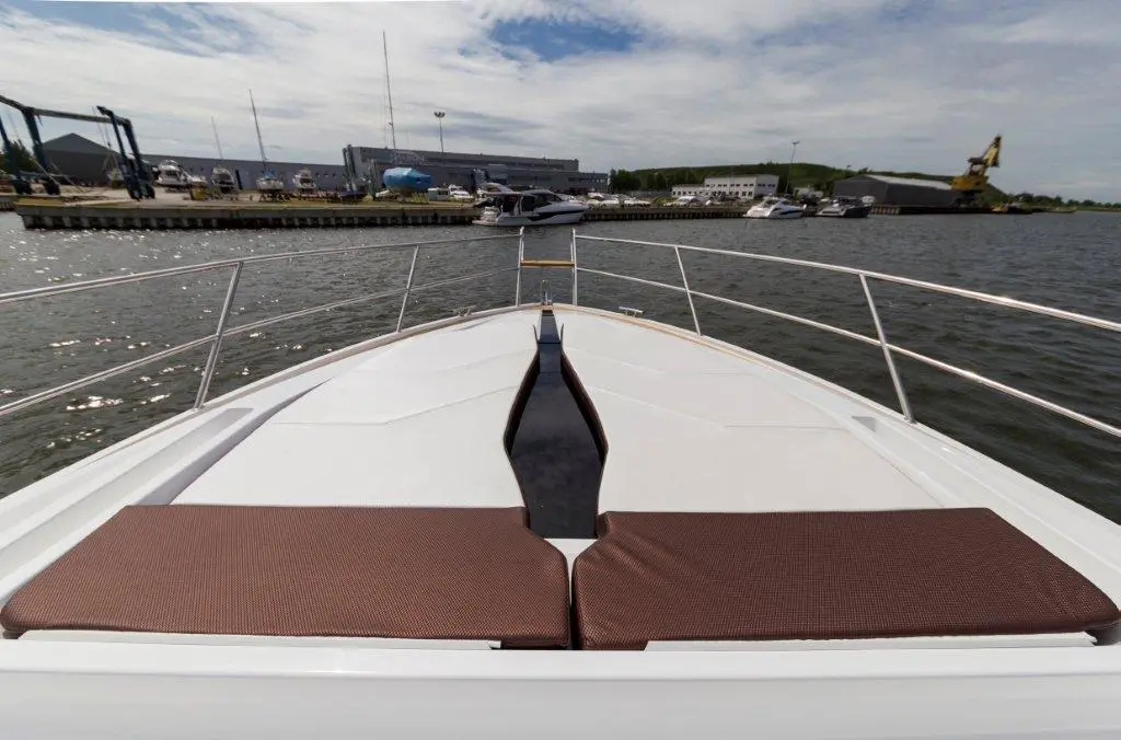 A view from the front of a yacht showing a brown cushioned seating area overlooking a marina with parked boats.