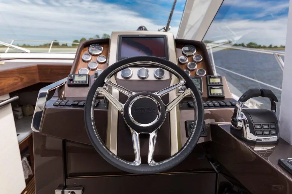 Luxury yacht helm featuring a sleek steering wheel, navigation displays, and controls against a serene water background.