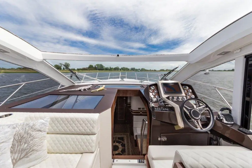 Luxurious yacht cockpit view with steering wheel, navigation controls, and water scenery under a blue sky.