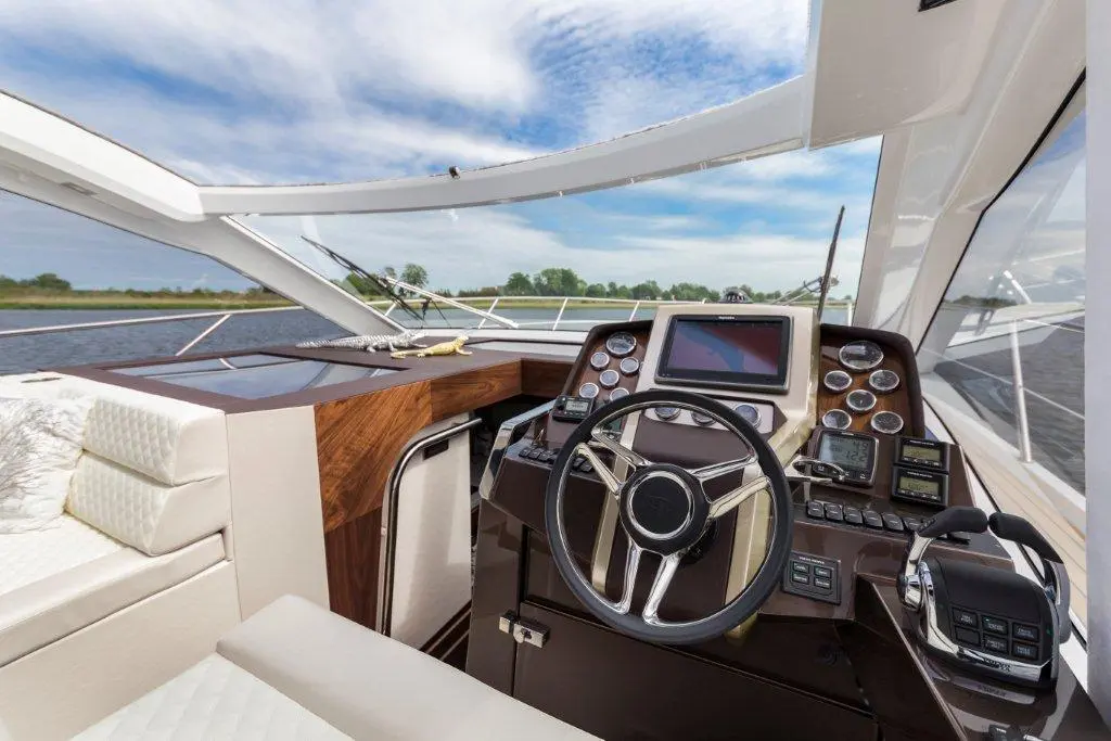 Luxury yacht interior showing a modern helm with steering wheel, dashboard, and plush seating against a scenic water backdrop.