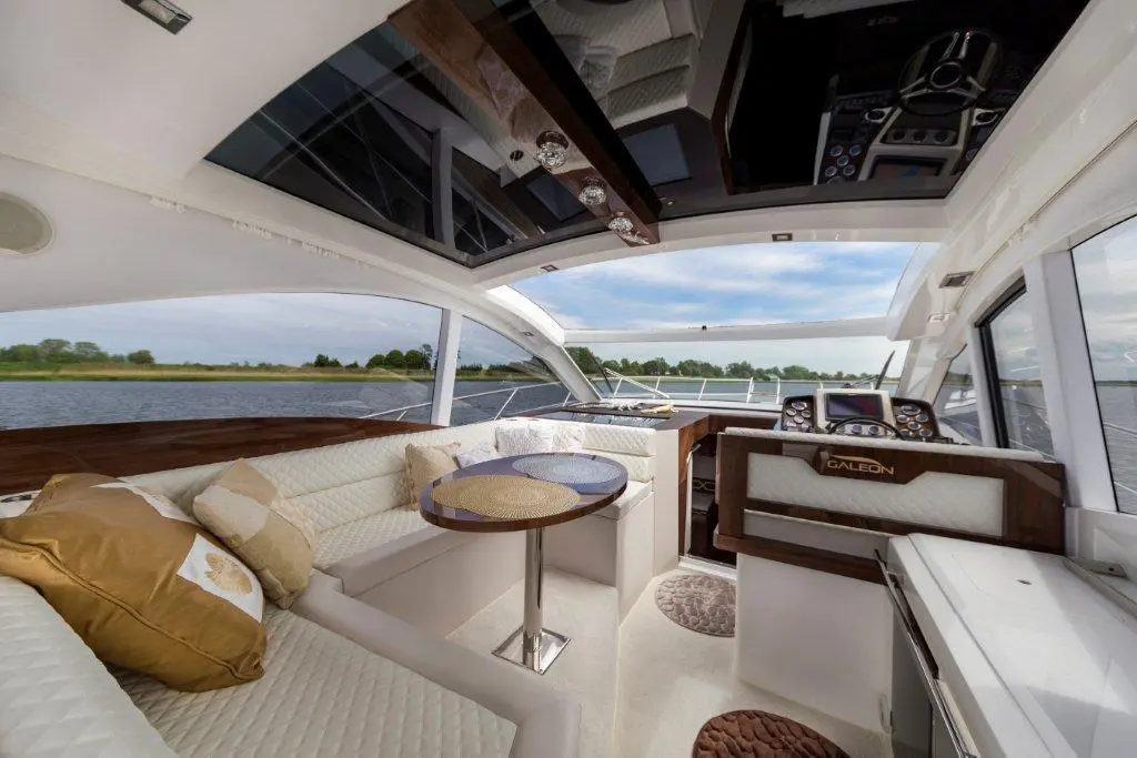 Luxurious yacht interior with a spacious lounge, circular table, and modern helm, overlooking a scenic waterway.