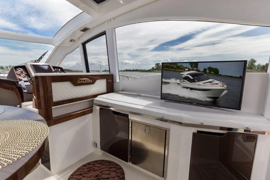 Interior of a luxury boat showing a sleek design, with a Galleon logo and a TV displaying a motorboat in motion.