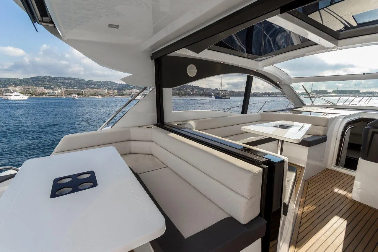 Luxurious yacht deck with white seating, a table, and panoramic views of the waterfront and distant hills under a clear sky.