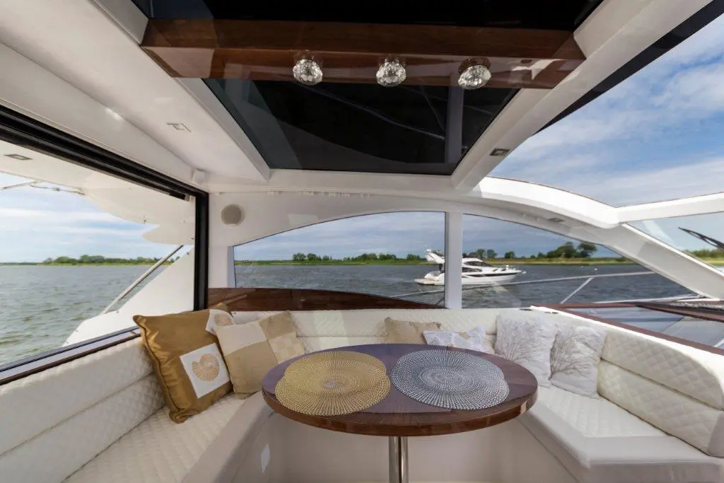Elegant boat interior features a round table, plush cushions, and scenic water views through large windows.