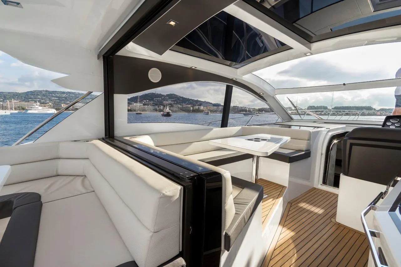 Modern yacht interior featuring plush seating, a sleek table, panoramic windows, and scenic views of the harbor.