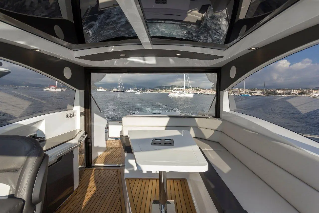 Modern boat interior features a table and seating area, showcasing a scenic view of water and yachts outside.