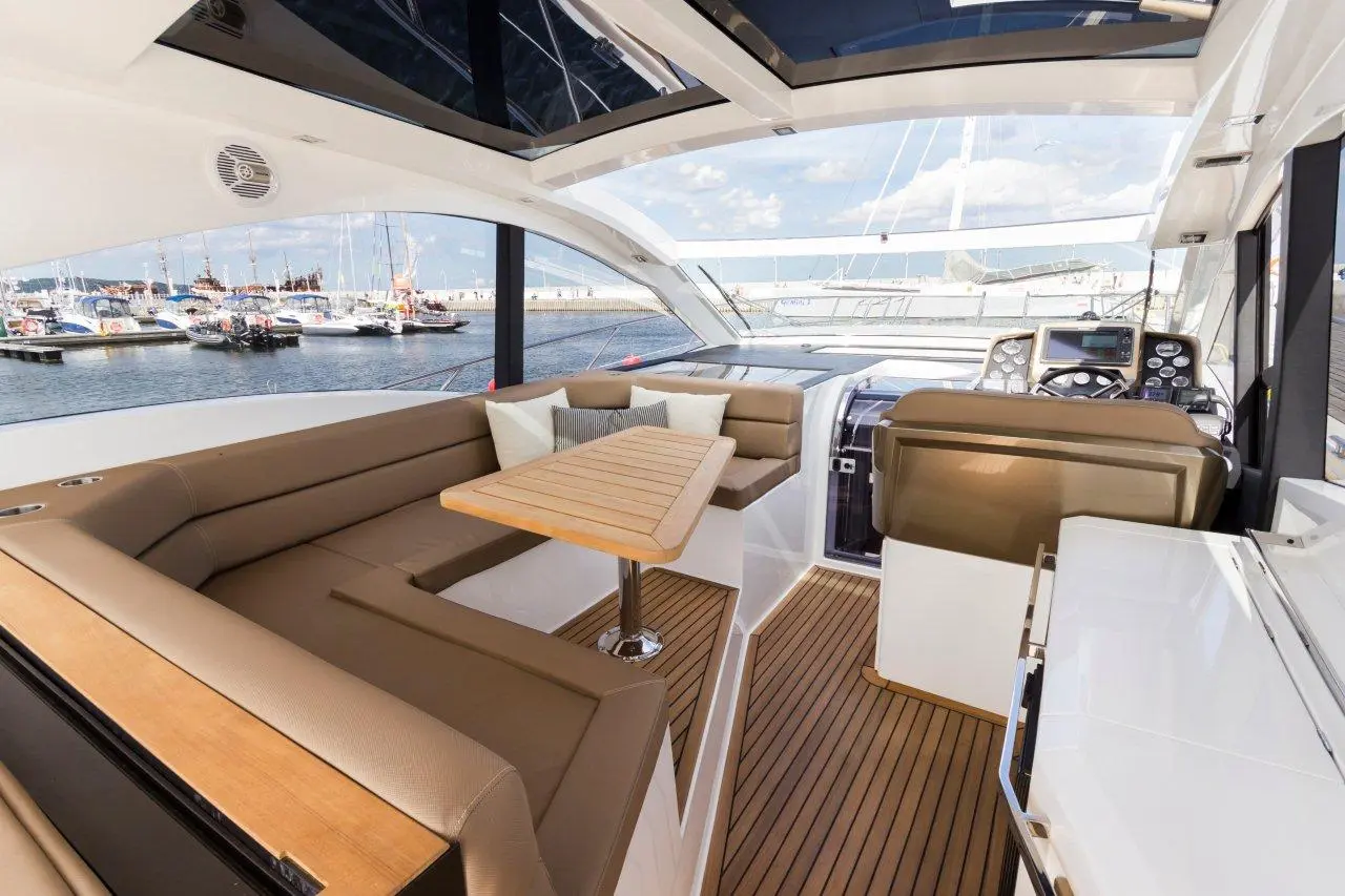 Luxury yacht interior featuring a wooden dining table, plush seating, and a view of the marina through large windows.