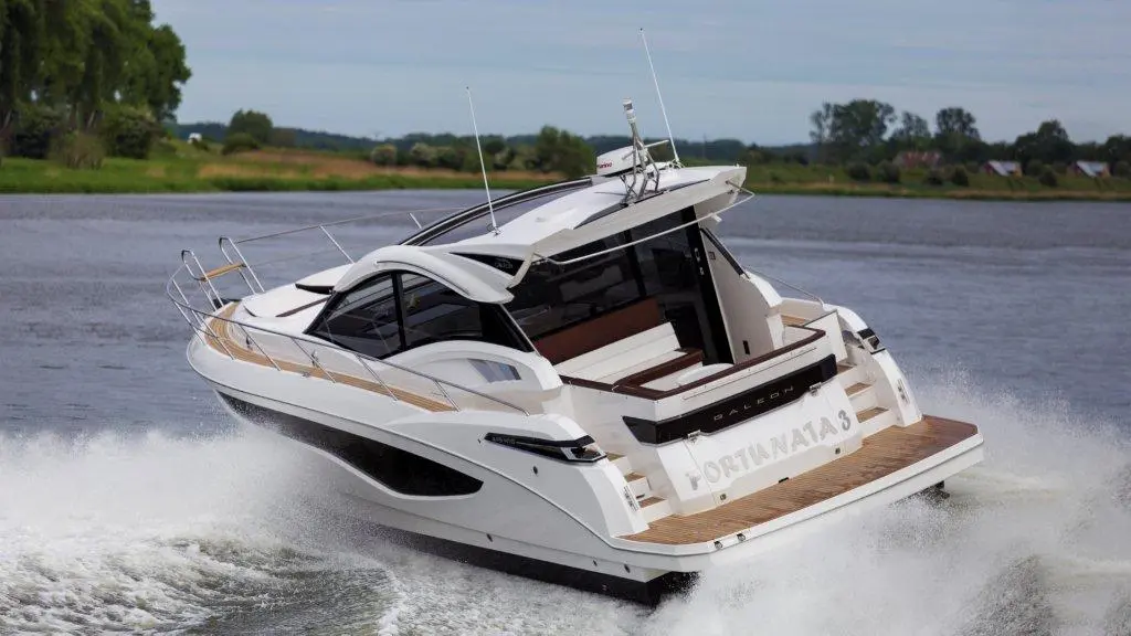 A sleek white motorboat with wooden accents speeding through water, displaying the name 
