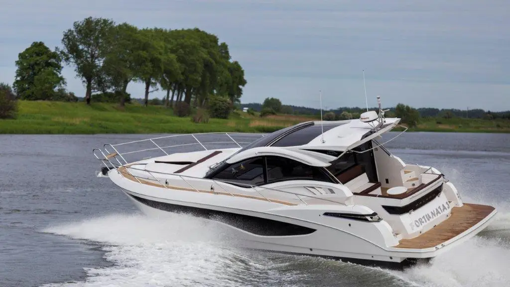 A sleek white motorboat speeds on a river, surrounded by green trees and calm waters, displaying the name 