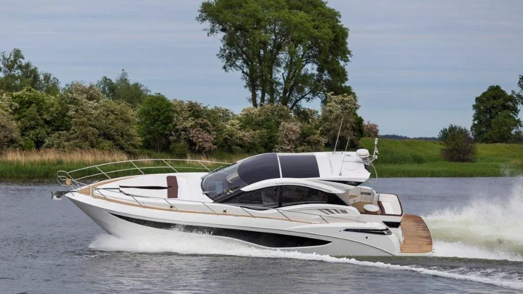 A sleek white motor yacht glides across a calm river, surrounded by lush greenery and soft clouds in a serene sky.