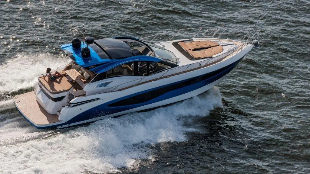 A sleek motor yacht with a blue top speeds through water, showcasing a tan cushioned deck and a relaxed passenger.