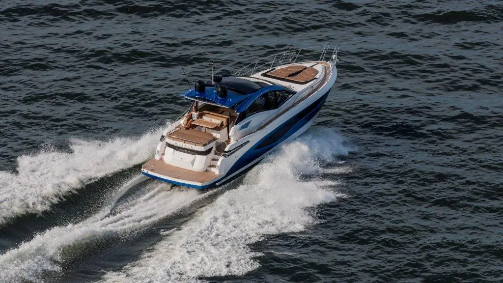 Luxury motorboat cruising on water, leaving white wakes; sleek design with blue and white exterior, outdoor seating visible.