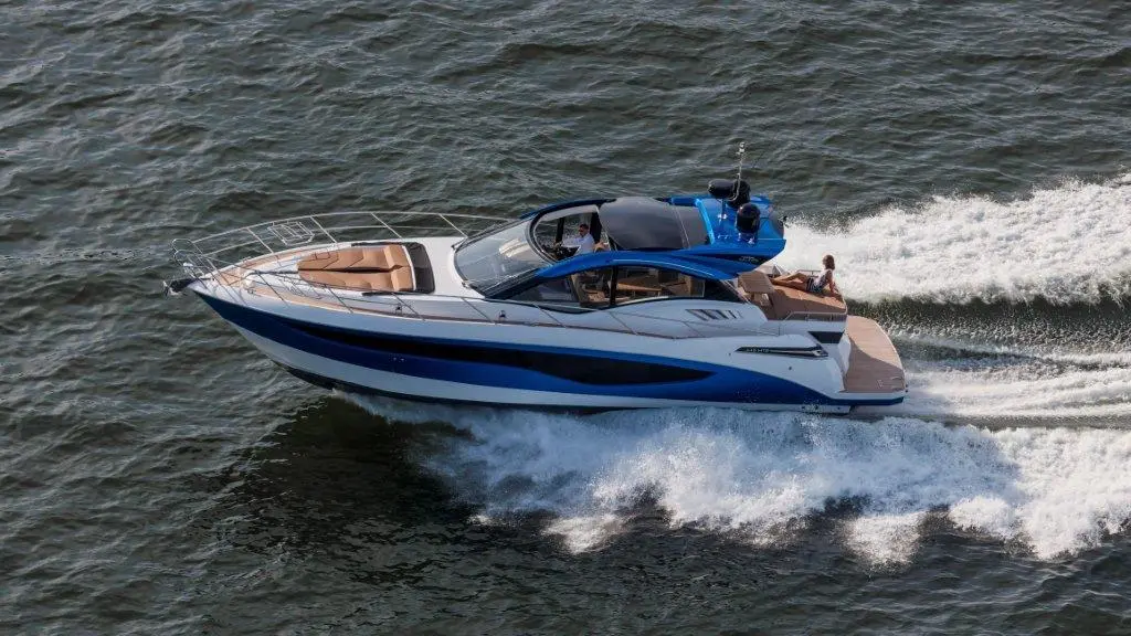 A blue and white motor yacht speeds across water, leaving wake behind while passengers enjoy the ride.