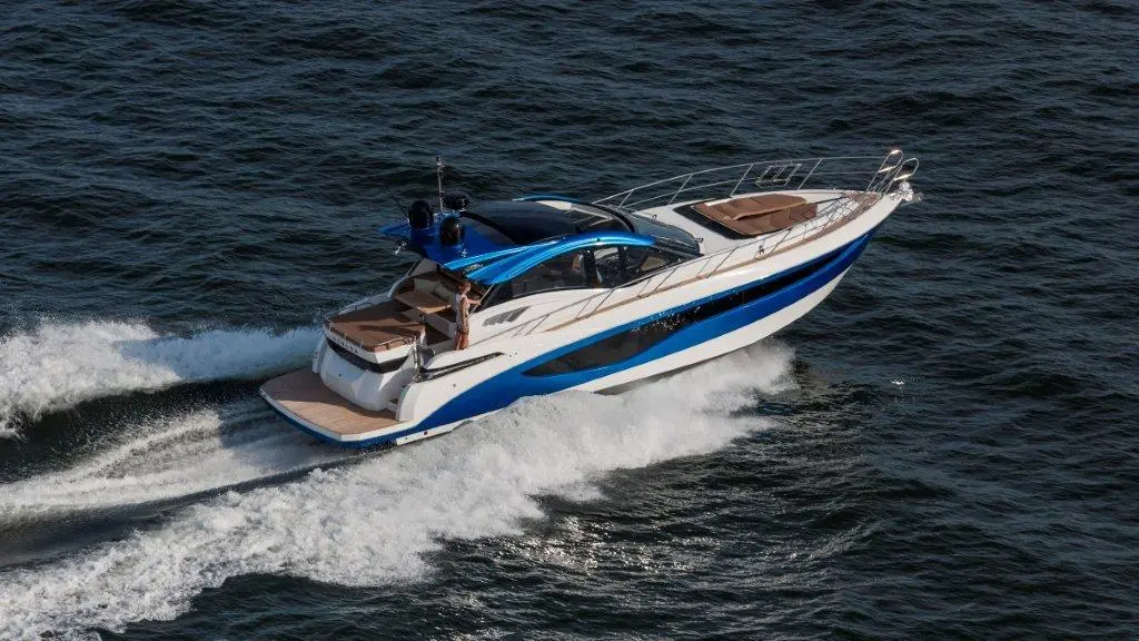 A luxurious white and blue motor yacht speeds across the water, creating waves behind it.