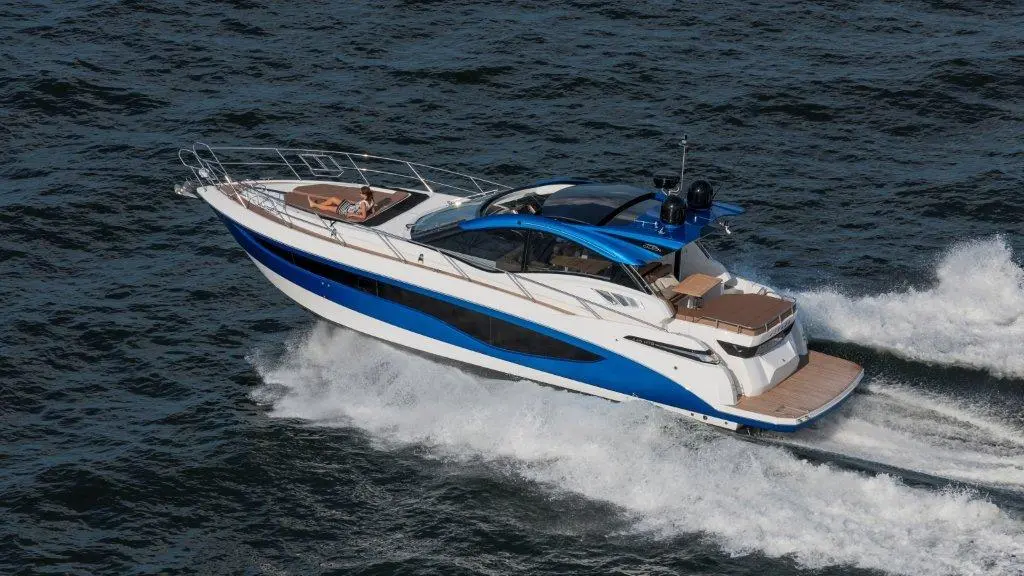 Luxury motorboat cruising on water, with a person relaxing on the deck, showcasing sleek design and vibrant blue accents.