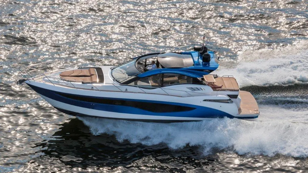 A sleek blue and white motor yacht glides through sparkling water, leaving a wake behind.