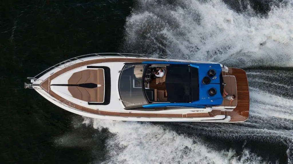 Aerial view of a luxury motorboat cruising on water, with two people on board and a wake trail behind.