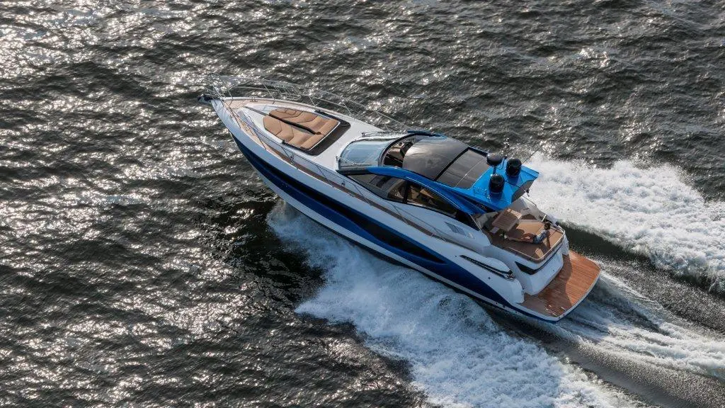A luxury motor yacht with a blue and white exterior glides over sparkling water, leaving a wake behind.