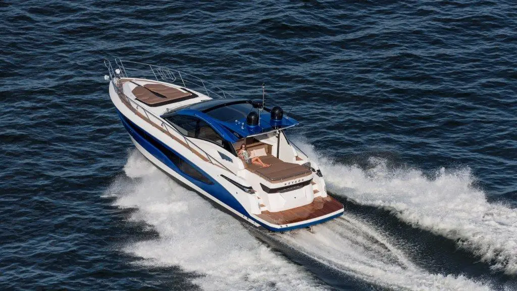 Luxury speedboat with a blue and white exterior glides over water, creating a wake on a sunny day.