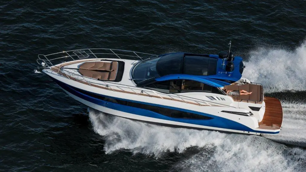 Luxury motor yacht cruising on waves, featuring brown seating area and a person relaxing on deck under sunlight.