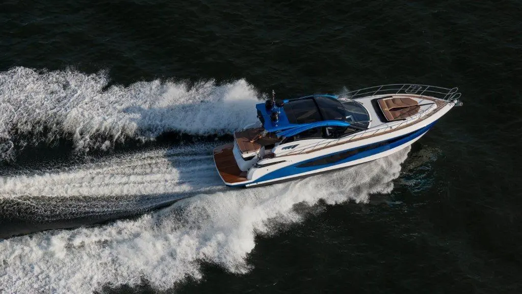 A blue and white luxury yacht cruising on choppy waters, leaving a trail of white foam in its wake.