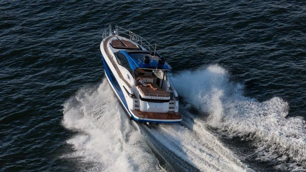 A luxury motor yacht speeds over the water, leaving a white wake against the dark blue waves.