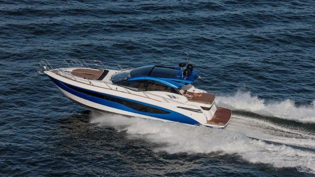 A sleek luxury motorboat with a blue and white design speeds through calm water, creating white waves behind it.