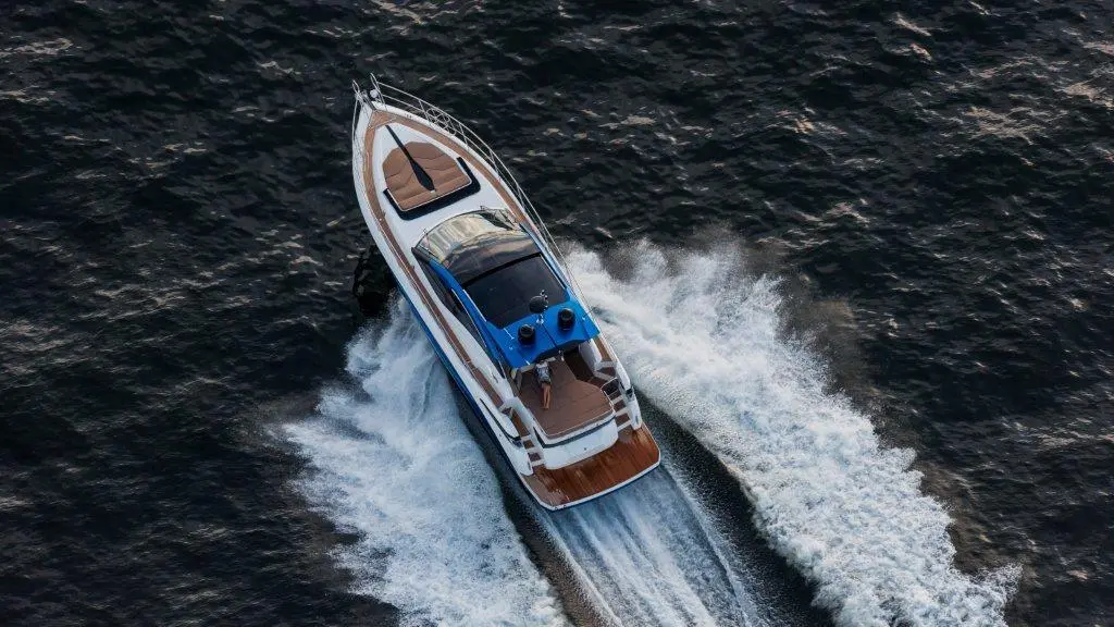 Aerial view of a sleek motorboat cutting through dark blue waters, leaving a white wake behind it.