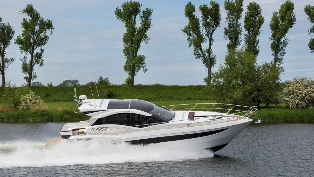 A sleek motorboat glides across a calm river, surrounded by lush green trees and a clear blue sky.