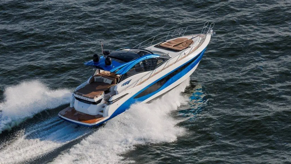 A sleek motorboat with a blue and white design speeds through water, creating waves and spray in a sunny environment.