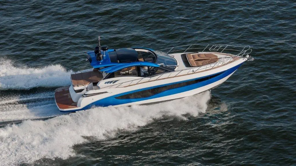 Luxury motorboat cruising through waves, featuring a sleek blue and white design, wooden deck, and sunbathing area.