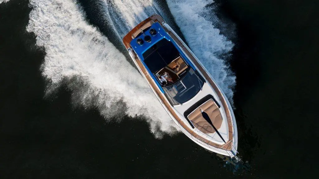 Aerial view of a motorboat speeding through dark waters, leaving a wake behind, with a person at the helm.
