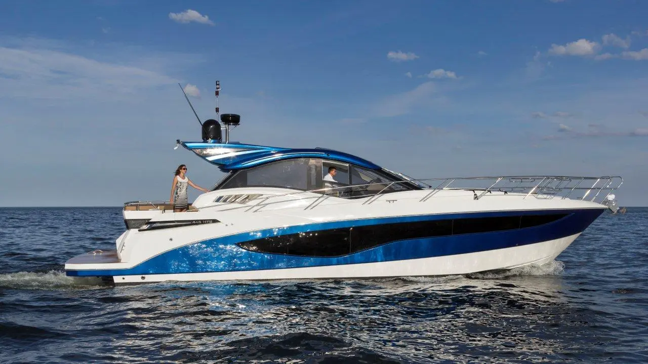 Luxury motor yacht with a blue and white design, cruising on calm water, featuring a woman on deck and a man at the helm.