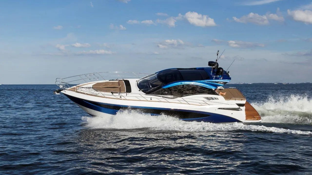 A sleek motorboat with a blue and white design speeds across calm waters under a clear sky, creating a wake.
