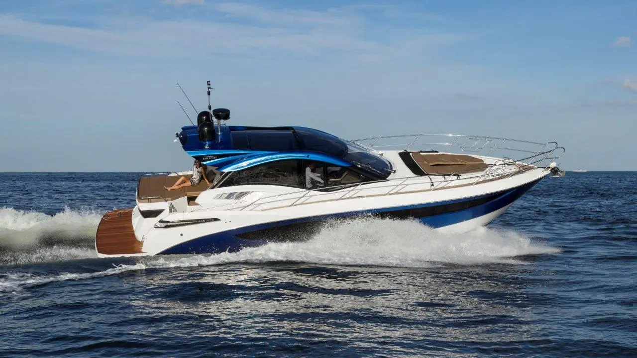 A sleek powerboat cruising through calm waters, with a person relaxing on deck under a blue sky, showcasing luxury.