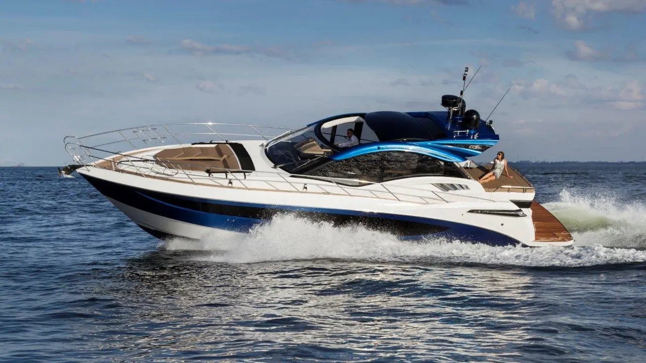 A motor yacht with a sleek blue and white design speeds across calm water, featuring a woman relaxing on the deck.